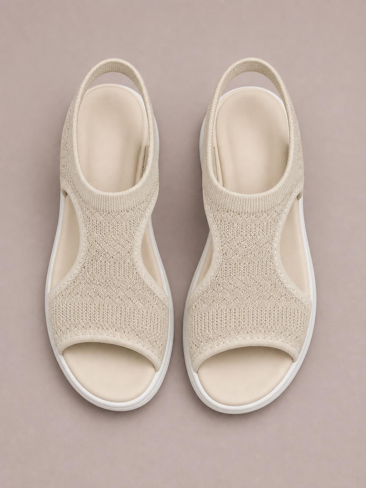 Solid beige peep toe sandals feature woven cloth uppers, open sides, slingback straps, cushioned footbeds, and flat rubber soles.