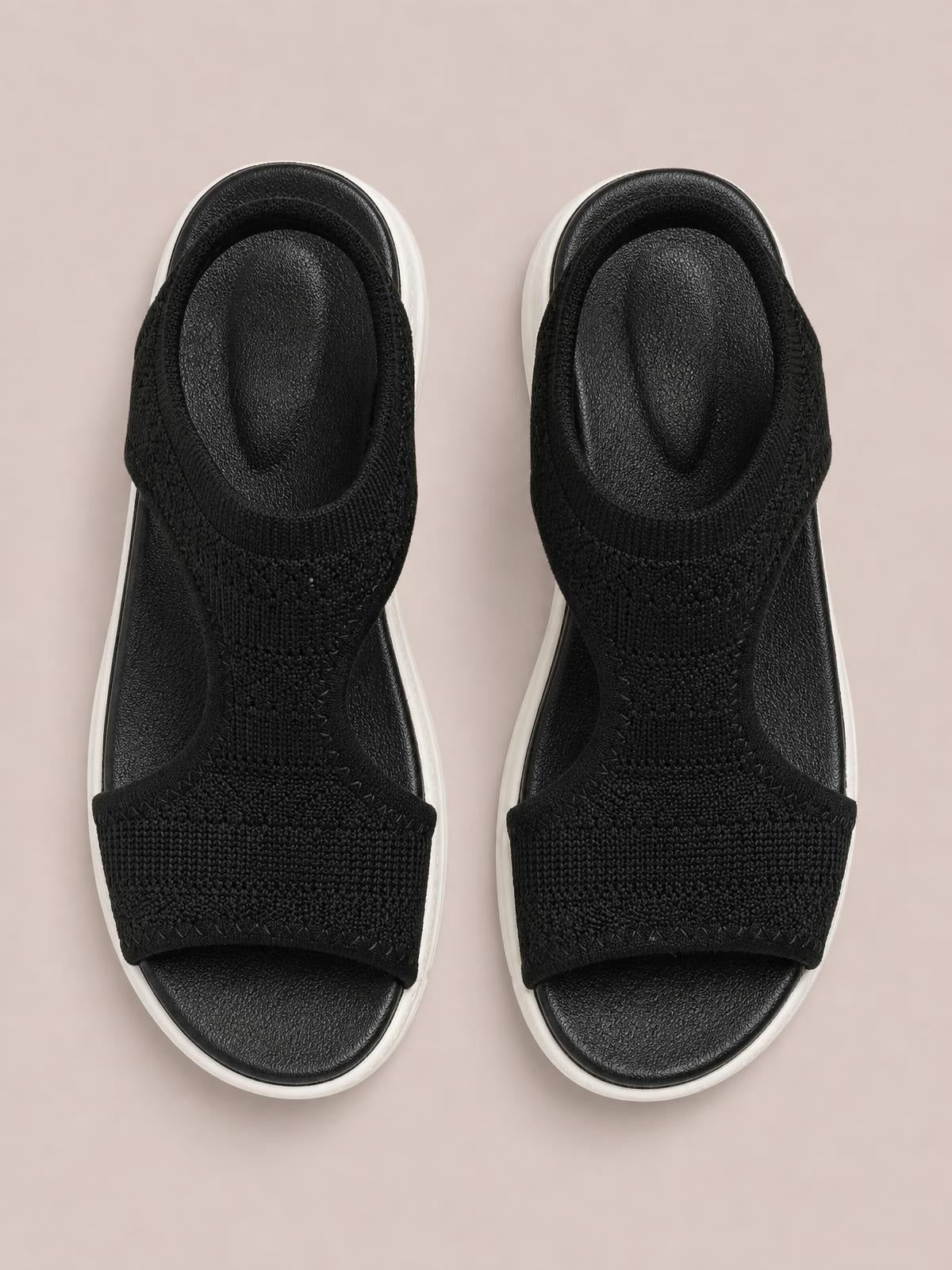 Black solid-color peep-toe flat sandals with wide woven cloth straps, textured footbeds, and contrasting white rubber soles, shown from above.