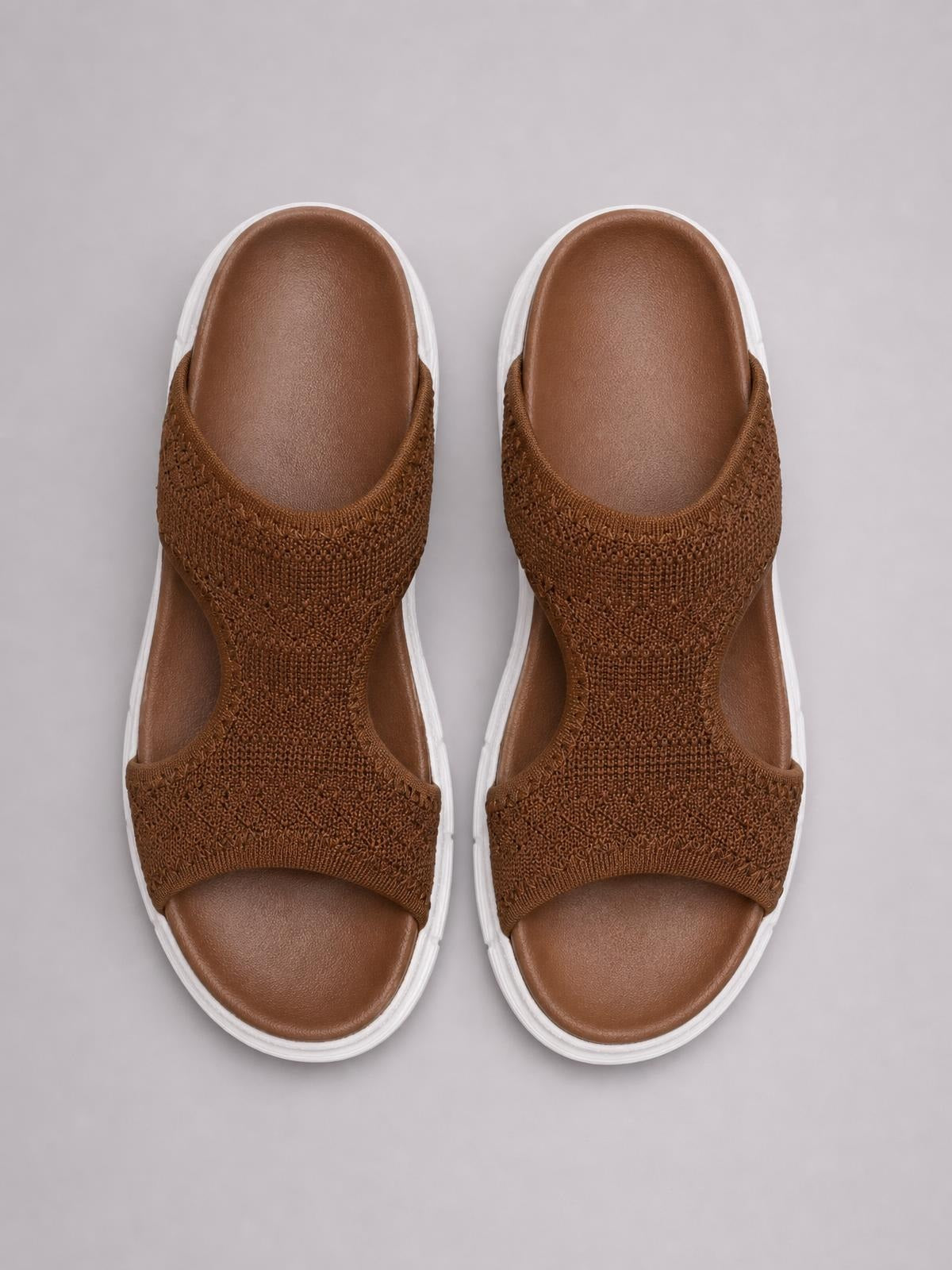 Brown solid-color peep-toe sandals with textured woven cloth straps, open sides, cushioned footbeds, and flat white rubber soles.