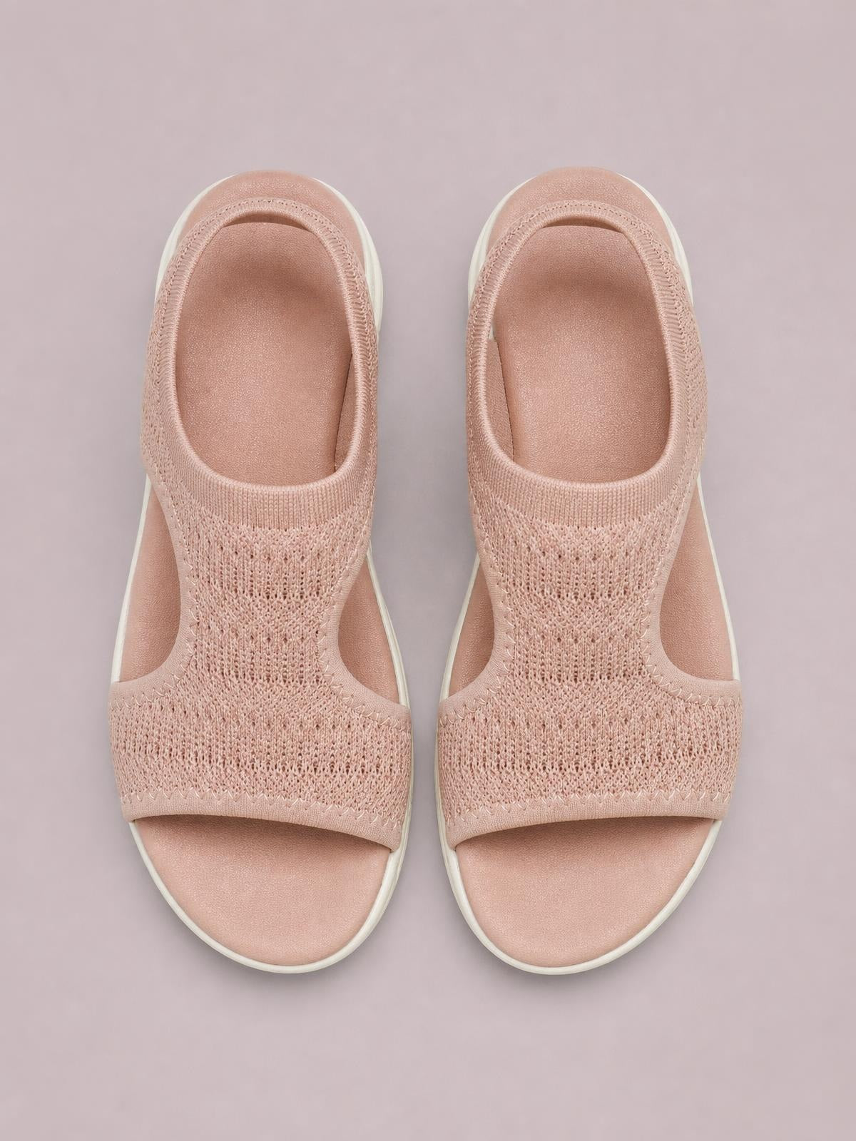 Blush pink peep-toe flat sandals feature breathable knit cloth uppers, open side panels, cushioned footbeds, and contrasting white rubber soles.