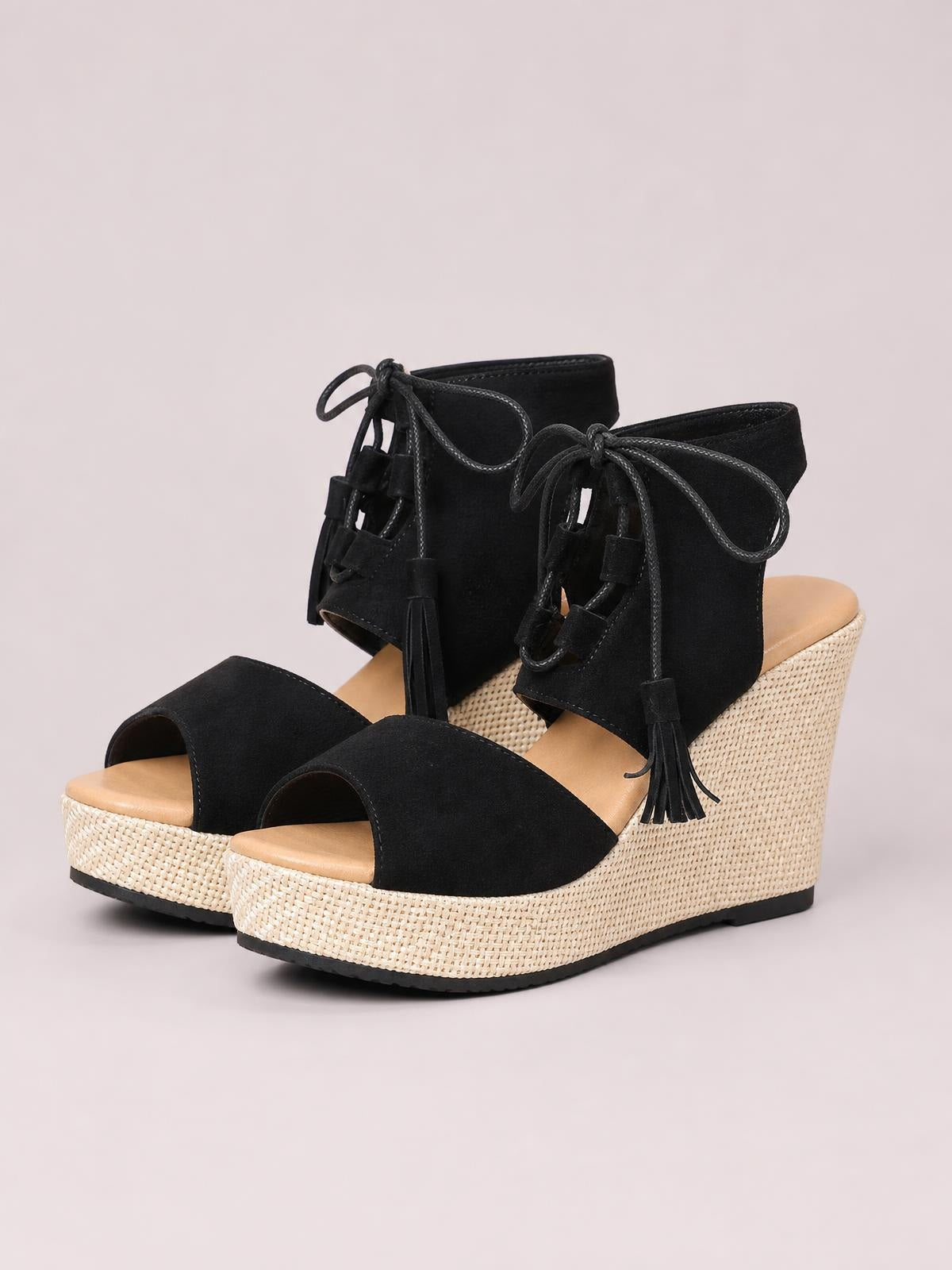 Black suede peep toe wedge sandals feature lace-up ankle straps with tassel details, tan footbeds, and textured woven mid-height wedge heels.