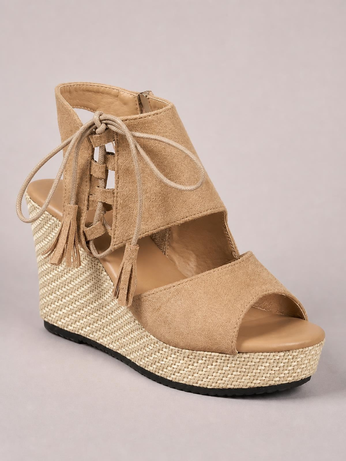 Tan suede peep toe wedge sandals with ankle laces, tassel accents, an open side design, and a woven mid-height wedge sole.