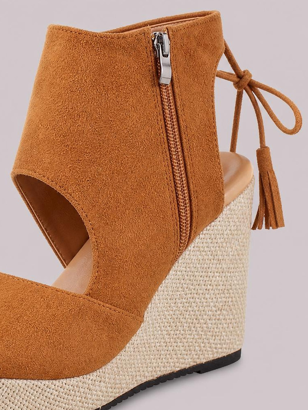 Close-up of a camel suede peep toe wedge sandal with a tall ankle upper, side zipper, tie tassels, woven espadrille mid-heel, and rubber sole.