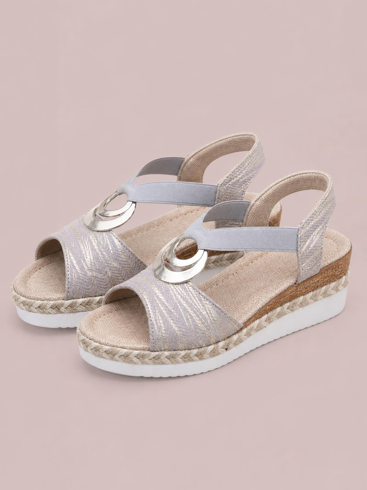 Lavender peep toe wedge sandals feature wide patterned straps, metallic circular accents, ankle straps, braided espadrille-style midsoles, and white rubber soles.