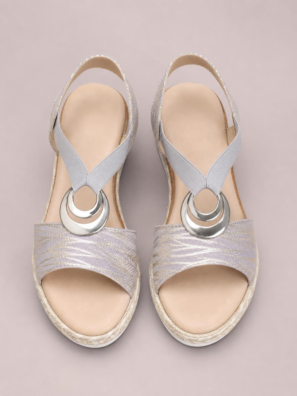 Silver peep toe wedge sandals feature crisscross straps, layered circular metallic embellishments, patterned textile uppers, and braided mid-height wedge soles.
