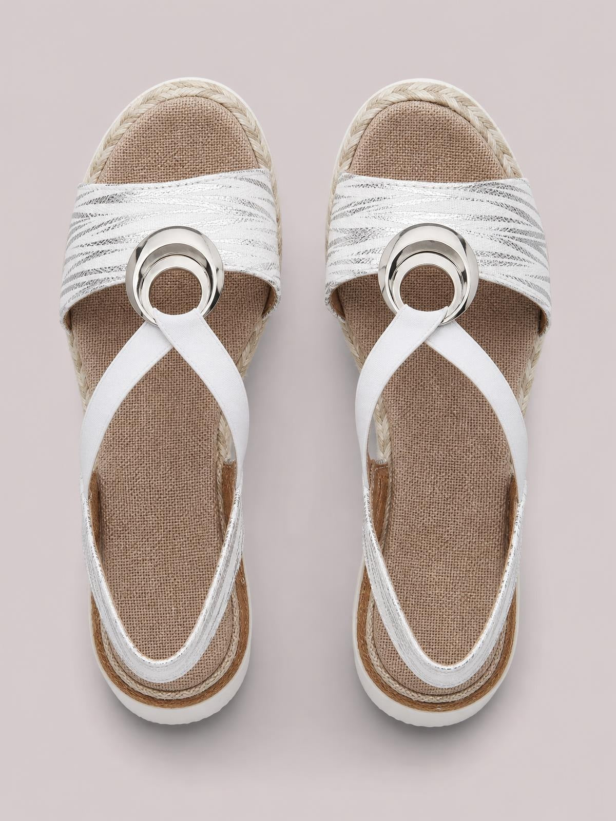 White peep-toe wedge sandals feature crisscross straps, circular metallic accents, textured insoles, and layered braided midsoles with a rubber outsole.