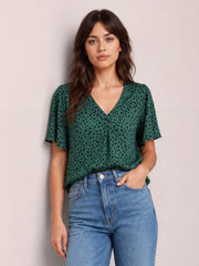 Model wearing a green leopard-print V-neck blouse with short flutter sleeves and a relaxed regular-length silhouette, posing with one hand in her jeans pocket.