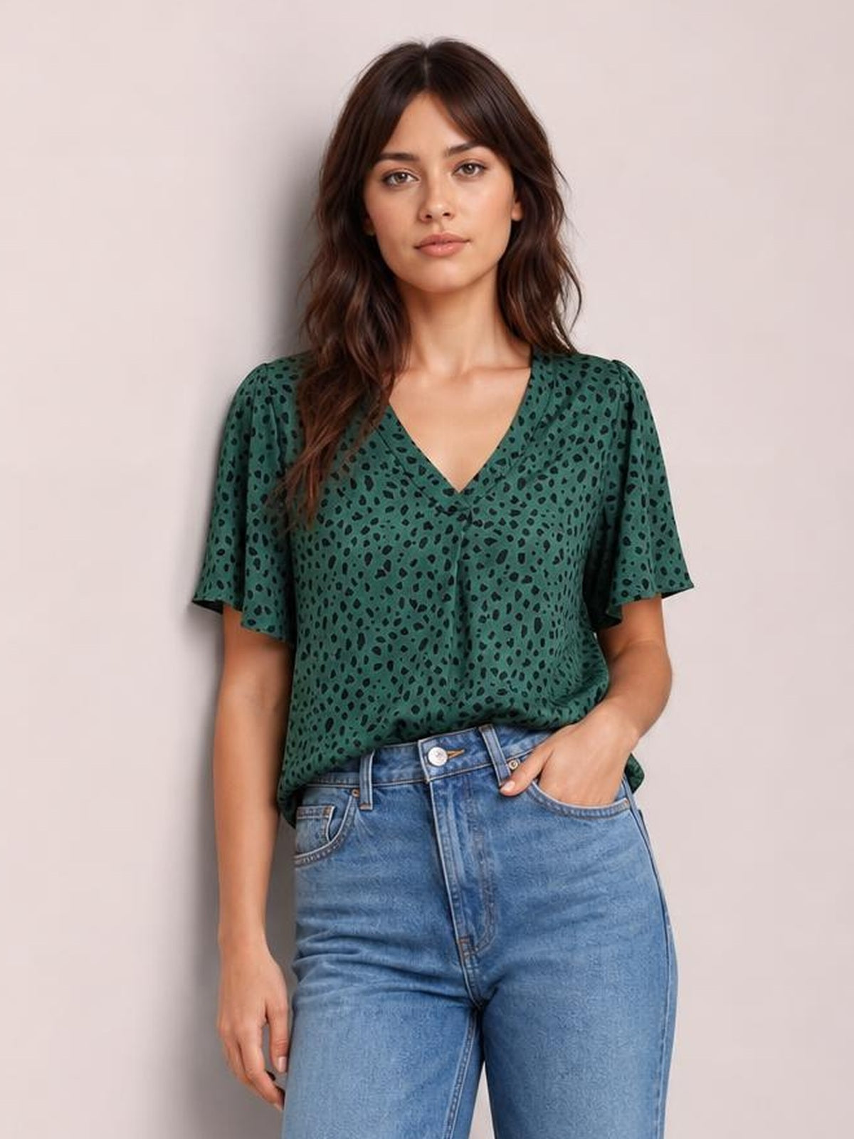 Model wearing a green leopard-print V-neck blouse with short flutter sleeves and a relaxed regular-length silhouette, posing with one hand in her jeans pocket.