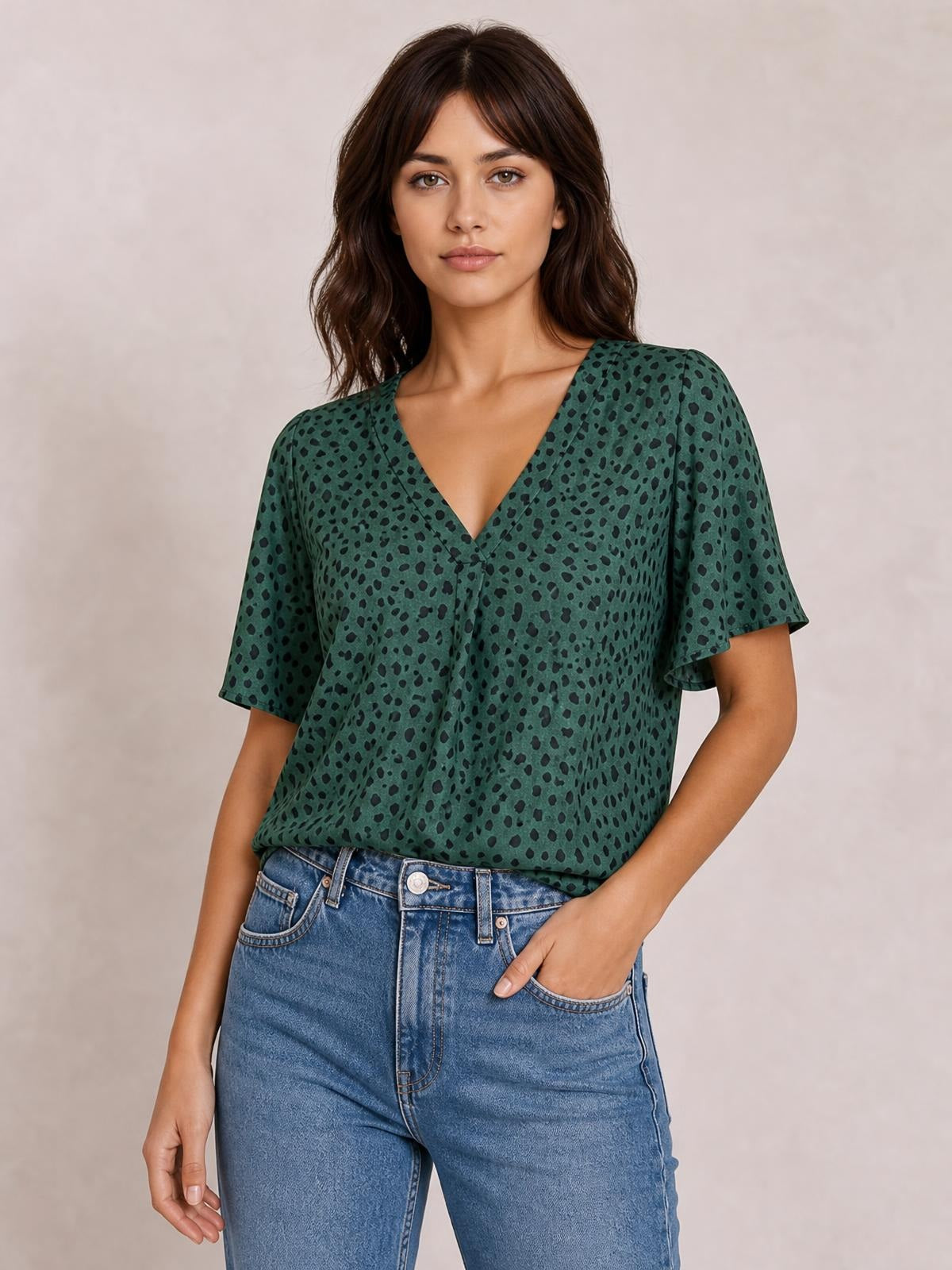 A model wears a green leopard-print V-neck blouse with short flutter sleeves and a relaxed regular silhouette, tucked into jeans with one hand in a pocket.