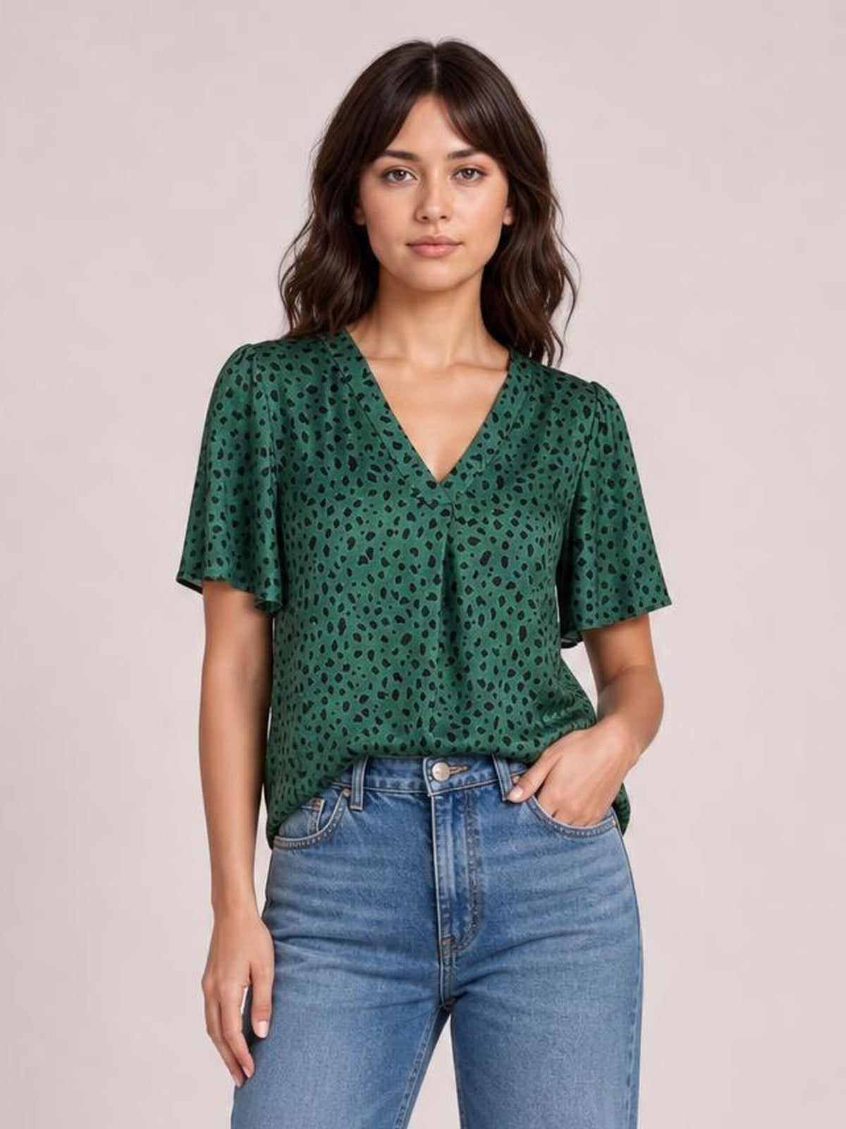 A model stands in a green leopard print blouse with a V-neck, short flutter sleeves, and a relaxed regular silhouette, one hand in her jeans pocket.