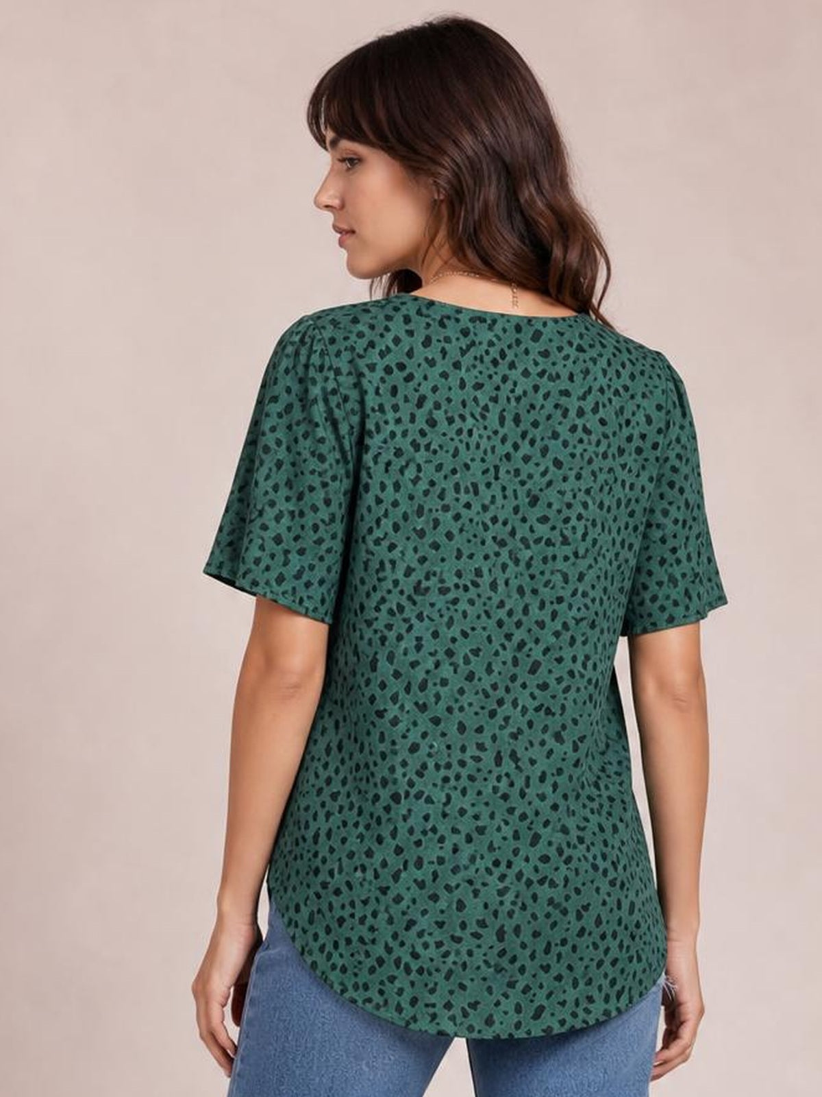 Model turned away wears a teal leopard-print blouse with short sleeves, a relaxed straight silhouette, and a curved hem over blue jeans.