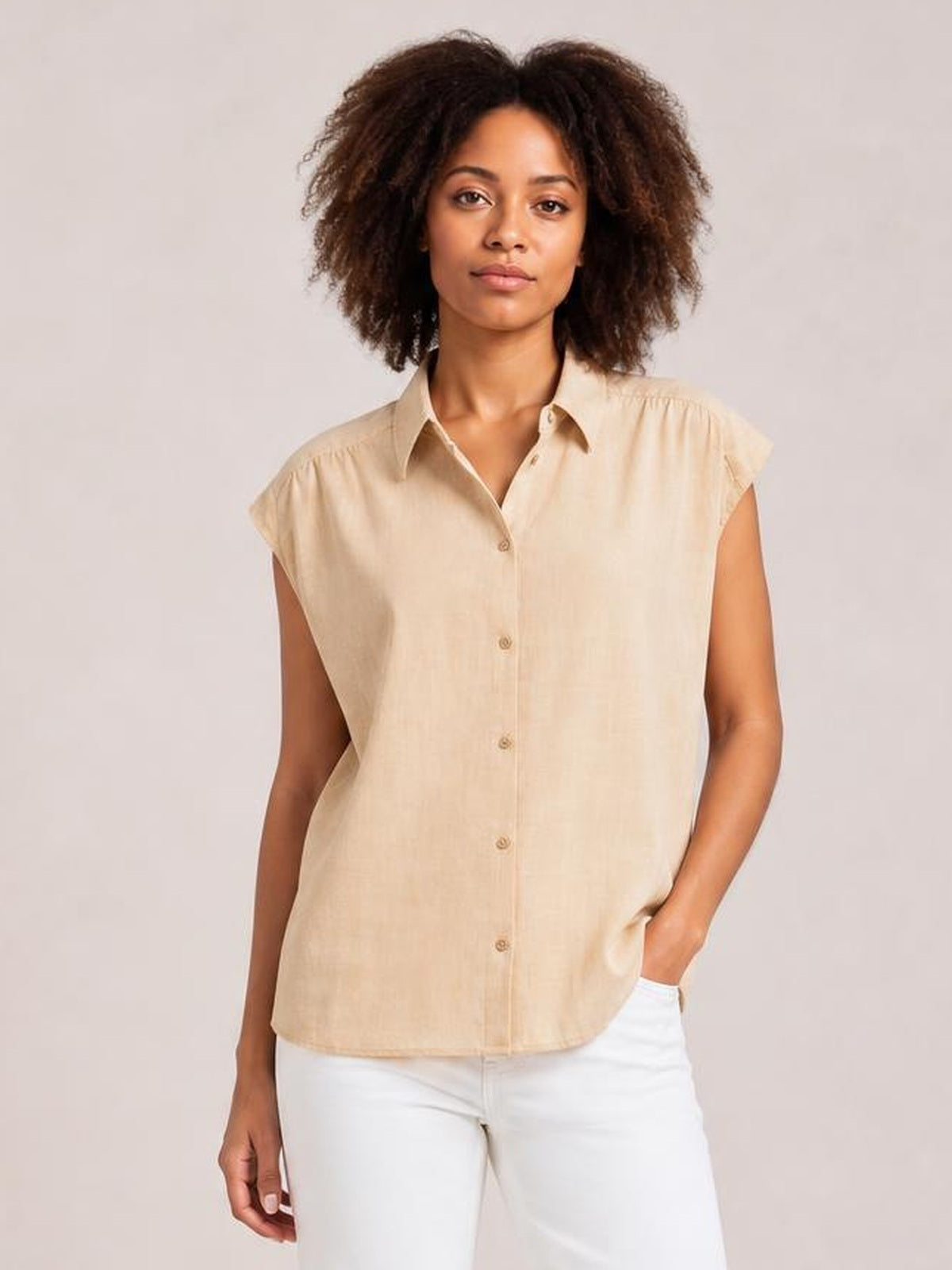 A model stands in a beige button-up shirt with a collared neck, cap sleeves, front buttons, and a relaxed straight silhouette.