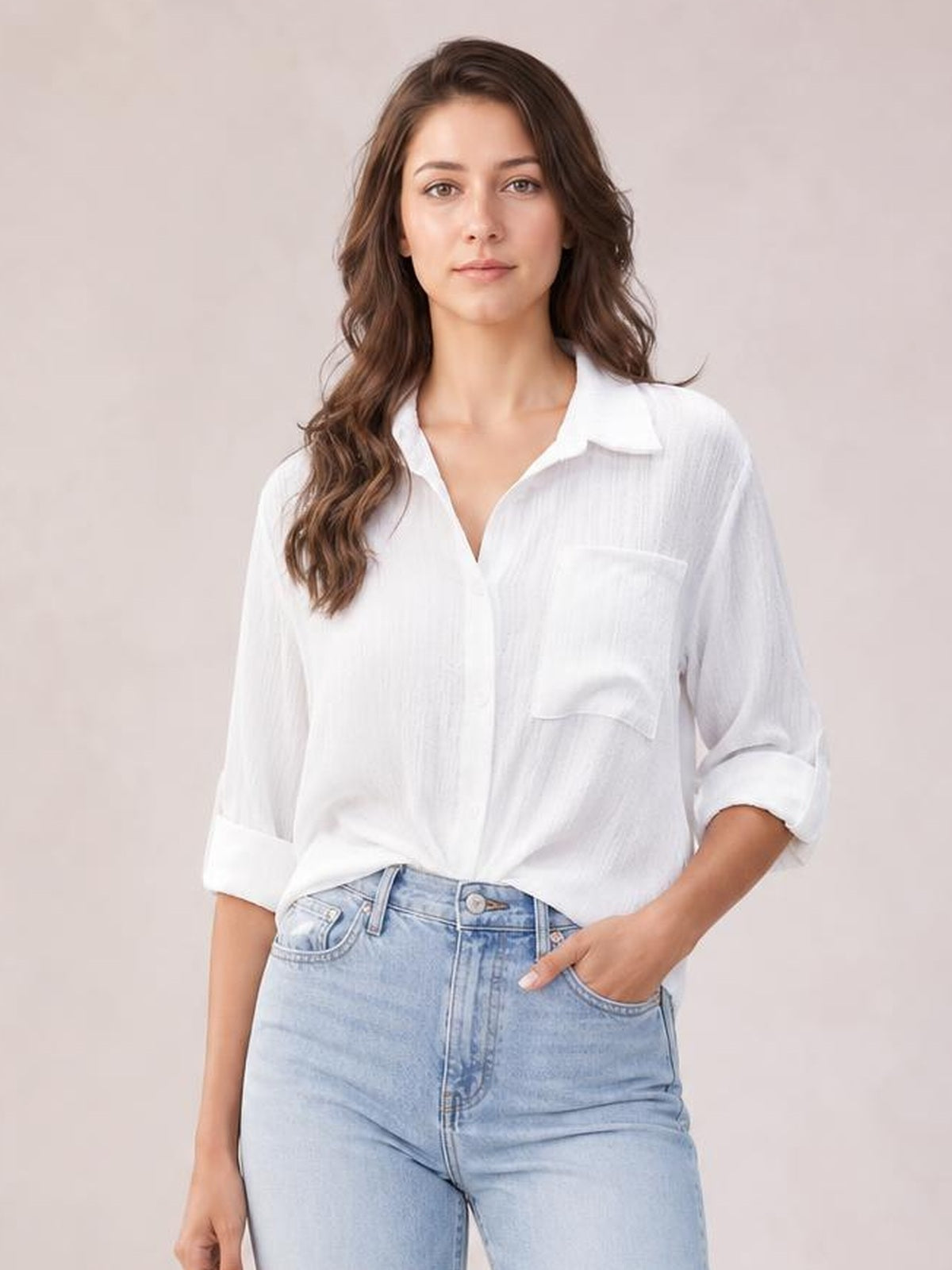 A model stands in a white collared neck twisted shirt with a relaxed silhouette, button front, chest pocket, and rolled three-quarter sleeves.
