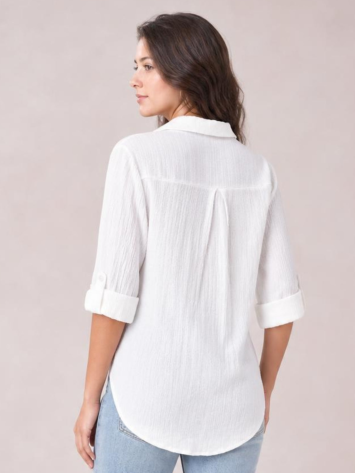 A model wears a white collared shirt with rolled three-quarter sleeves, a relaxed silhouette, back pleat, and curved regular hem.