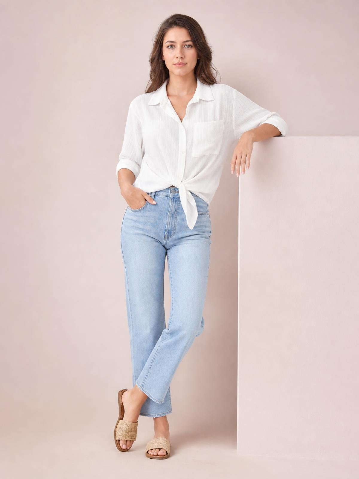 A model wears a white collared neck twisted shirt with three-quarter roll-tab sleeves and a tied front, standing casually in light-wash jeans.