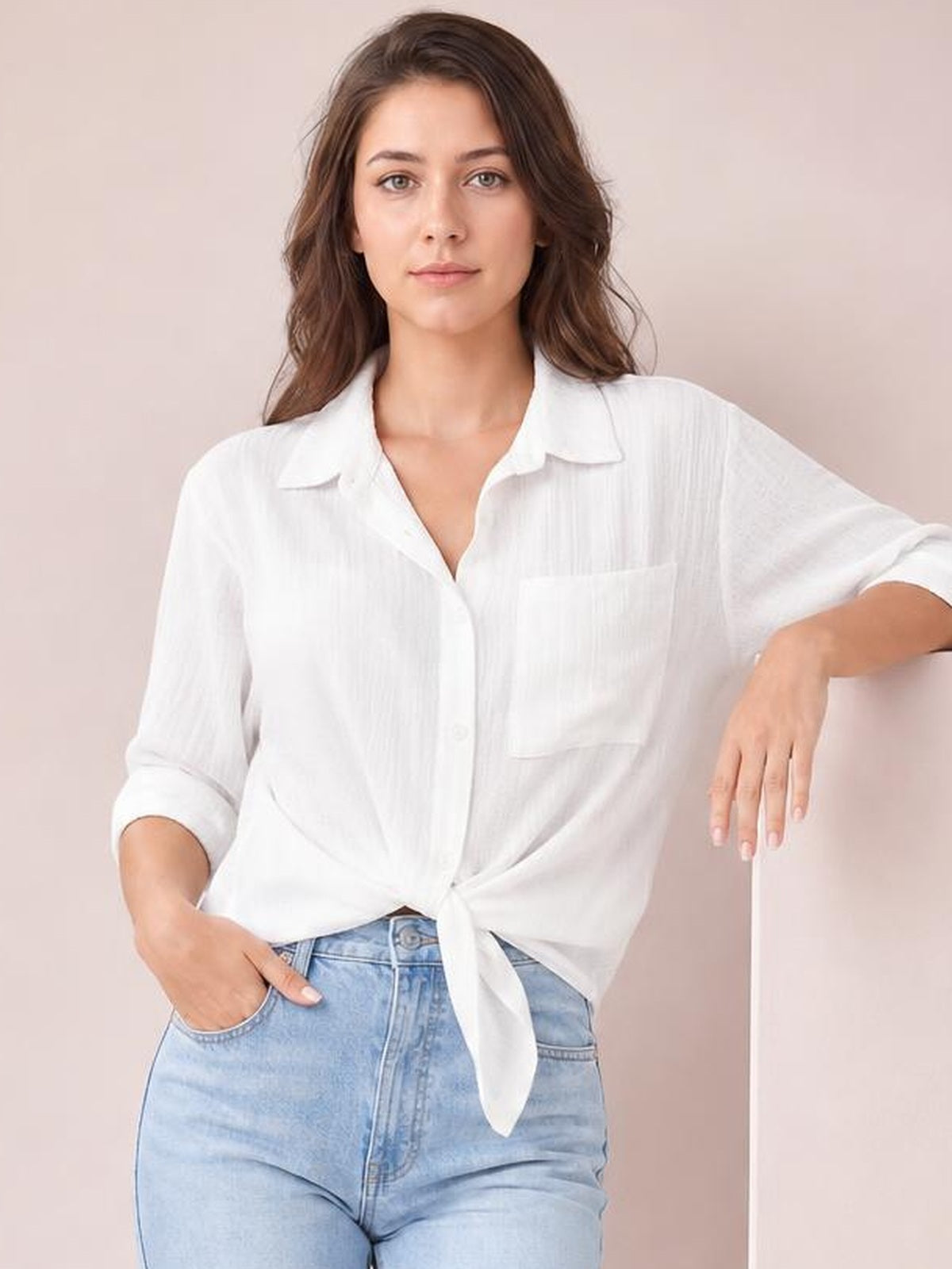 Model poses in a white solid collared shirt with three-quarter roll-tab sleeves, chest pocket, relaxed regular silhouette, and a tied front hem.