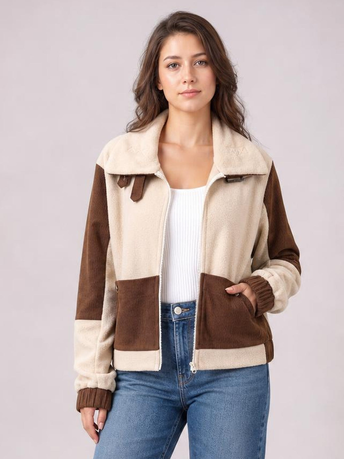 Model wears a beige and brown color block zip-up jacket with a collared neckline, ribbed cuffs, and front pockets, standing with one hand tucked inside.