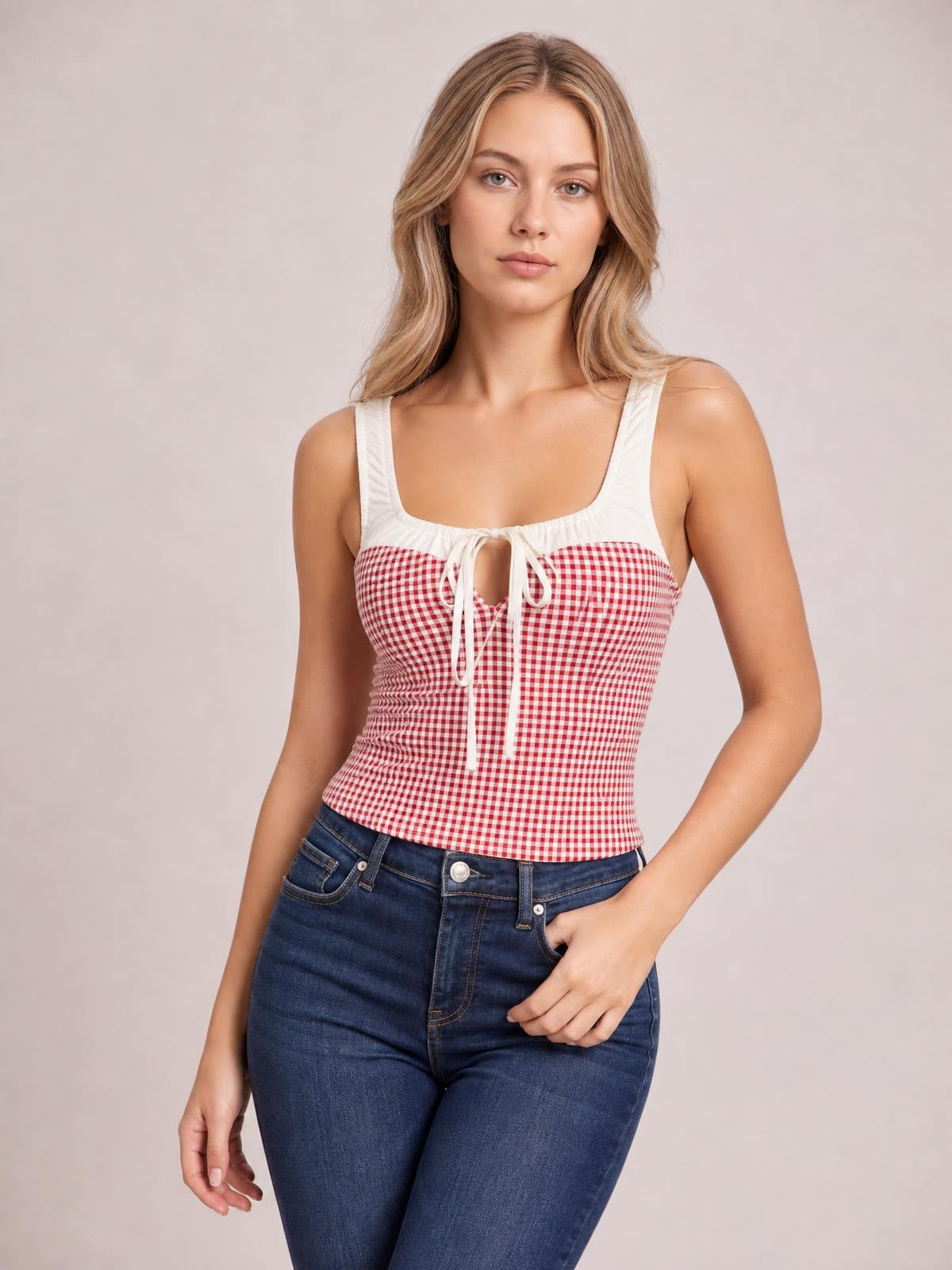 Model wears a fitted red-and-white contrast plaid tank with a square neckline, wide straps, white trim, and a front tie detail.