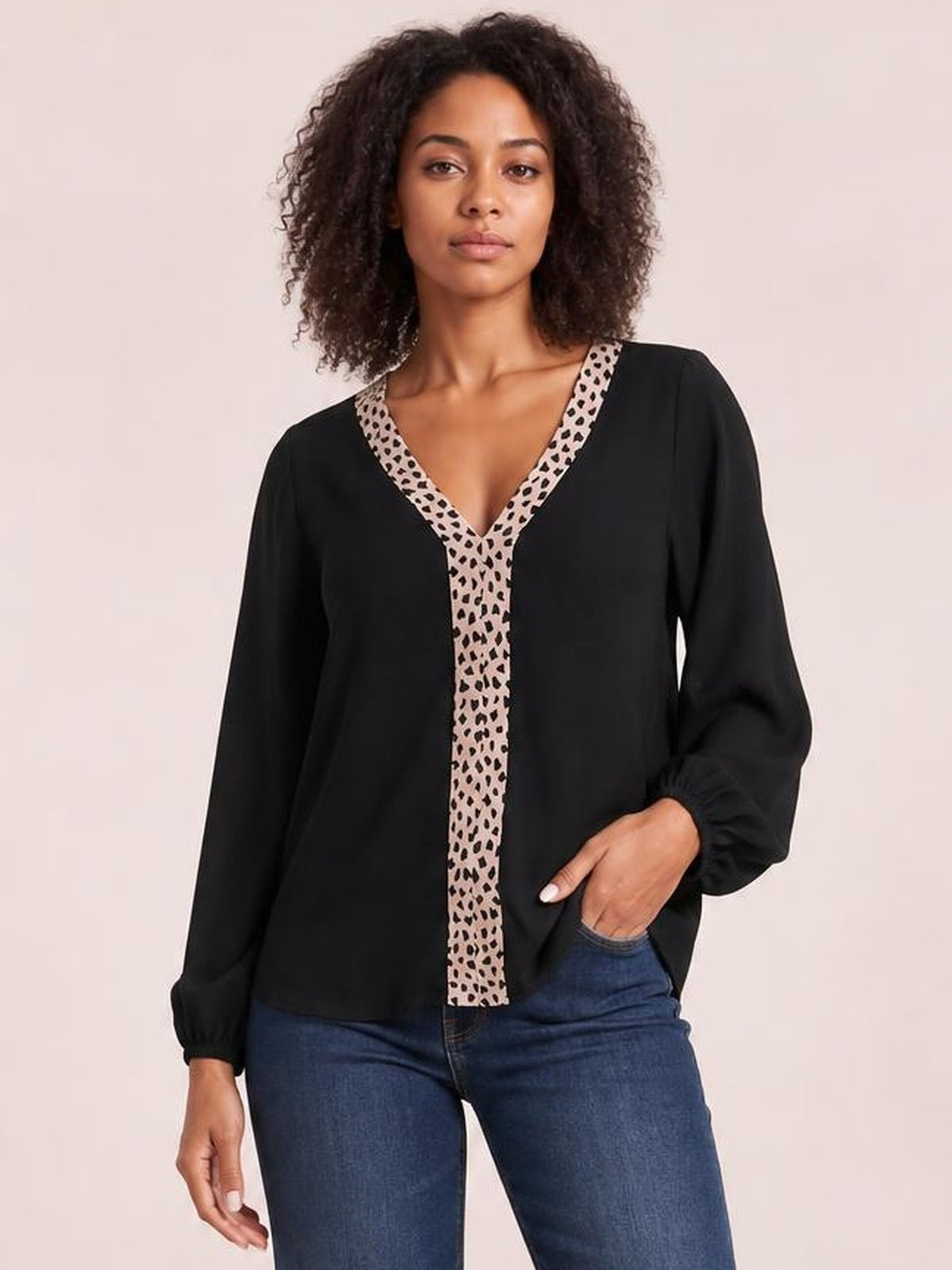 Model wearing a black contrast V-neck long sleeve blouse with a beige leopard-print trim, relaxed silhouette, and gathered cuffs, posed with one hand in her jeans pocket.