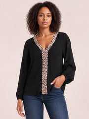 Model wearing a black contrast V-neck long sleeve blouse with a beige leopard-print trim, relaxed silhouette, and gathered cuffs, posed with one hand in her jeans pocket.