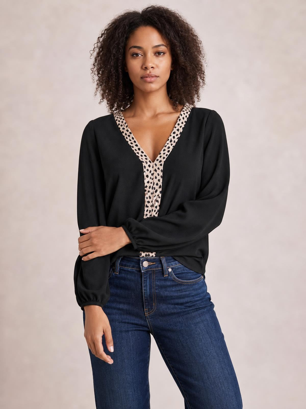 Model wears a black contrast V-neck long sleeve blouse with a leopard-print trim, relaxed silhouette, and gathered cuffs, posed with one arm across her waist.