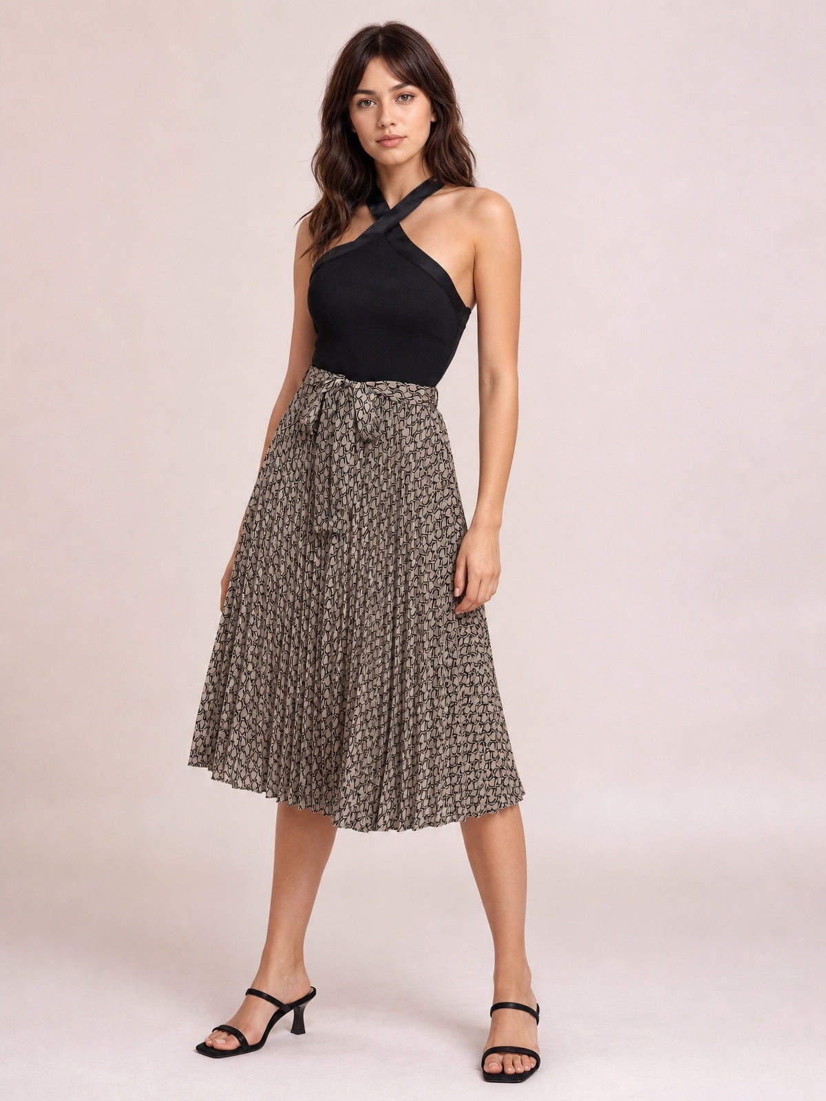 Model posing in a black crisscross halter neck dress with a solid fitted bodice, mocha printed gently flared skirt, and below-the-knee hem.