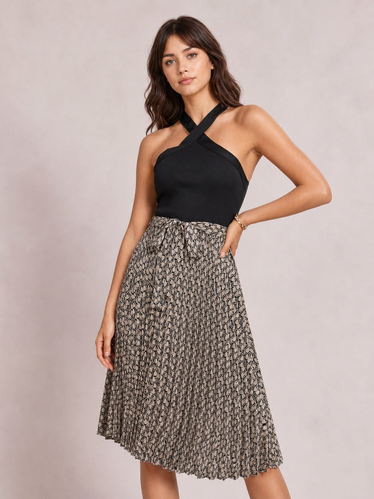 Model wearing a crisscross halter neck dress with a solid black bodice, mocha patterned gently flared skirt, and below-the-knee silhouette, posing with one hand on her hip.