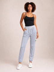 Model stands in a relaxed pose wearing light gray drawstring joggers with side pockets, an elastic waist, tapered legs, and cuffed ankles.