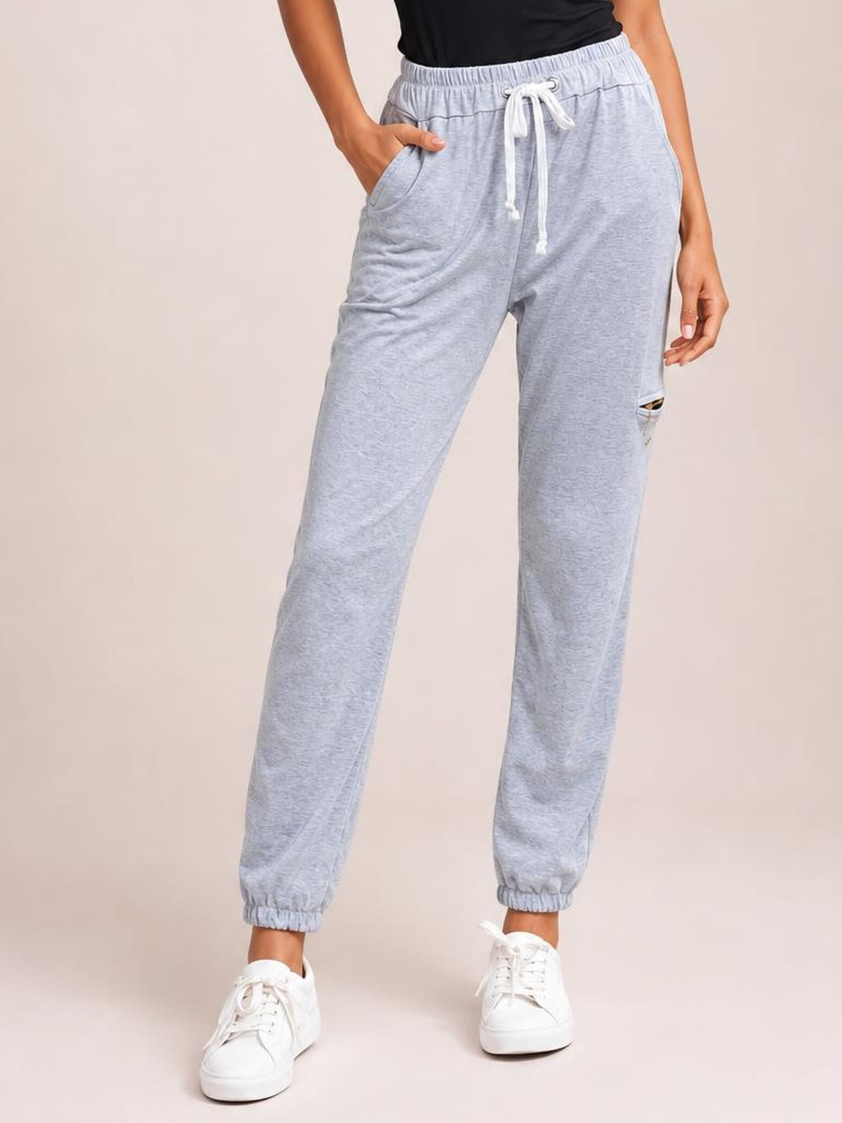 Model wears light gray drawstring joggers with side pockets, an elastic waistband and cuffs, standing with one hand tucked into a pocket.