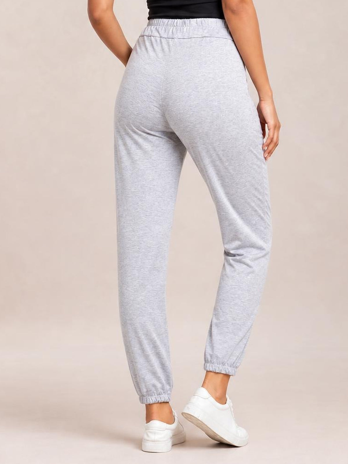 A model stands in a relaxed pose wearing light gray drawstring joggers with an elastic waist, roomy fit, tapered legs, and gathered ankle cuffs.