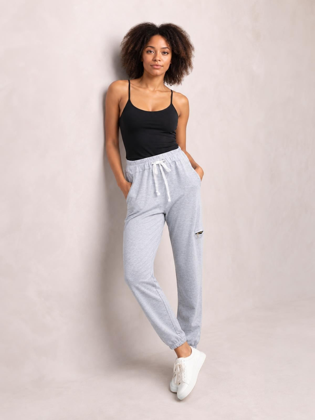 Model poses in light gray drawstring joggers with side pockets, an elastic waist, tapered legs, and cuffed ankles.
