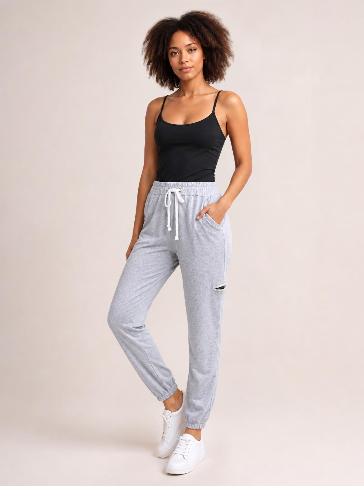 A model poses in light gray drawstring joggers with side pockets, an elastic waist and cuffs, and a relaxed tapered silhouette.