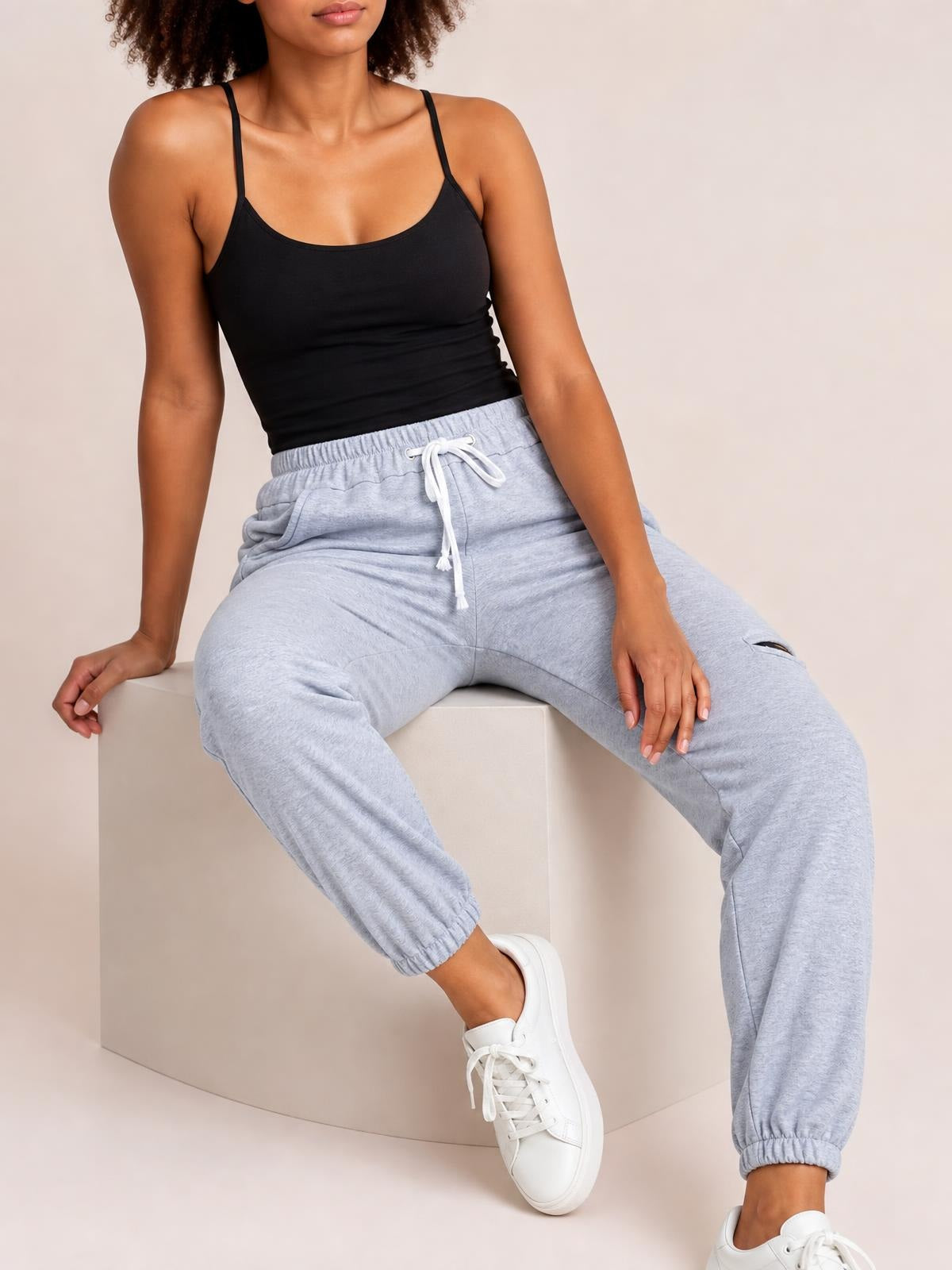 A seated model wears light gray drawstring joggers with a relaxed tapered silhouette, elastic cuffs, and practical side pockets.