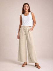 Model poses in beige drawstring wide leg pants with an elastic waist, front pockets, and a relaxed full-length silhouette.