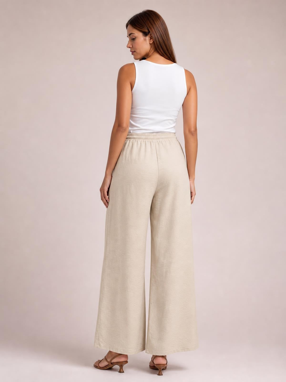 A model looks over her shoulder in beige wide-leg pants with a relaxed full-length silhouette and gathered elastic waistband.
