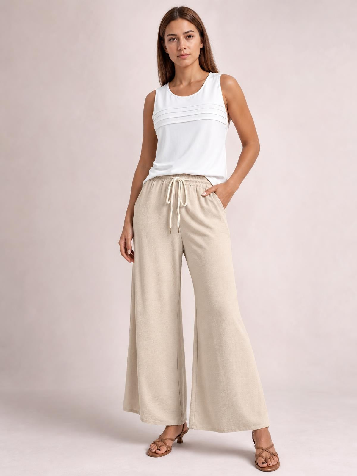 Model poses in beige drawstring wide leg pants with an elastic waistband, front pockets, and a flowing full-length silhouette.