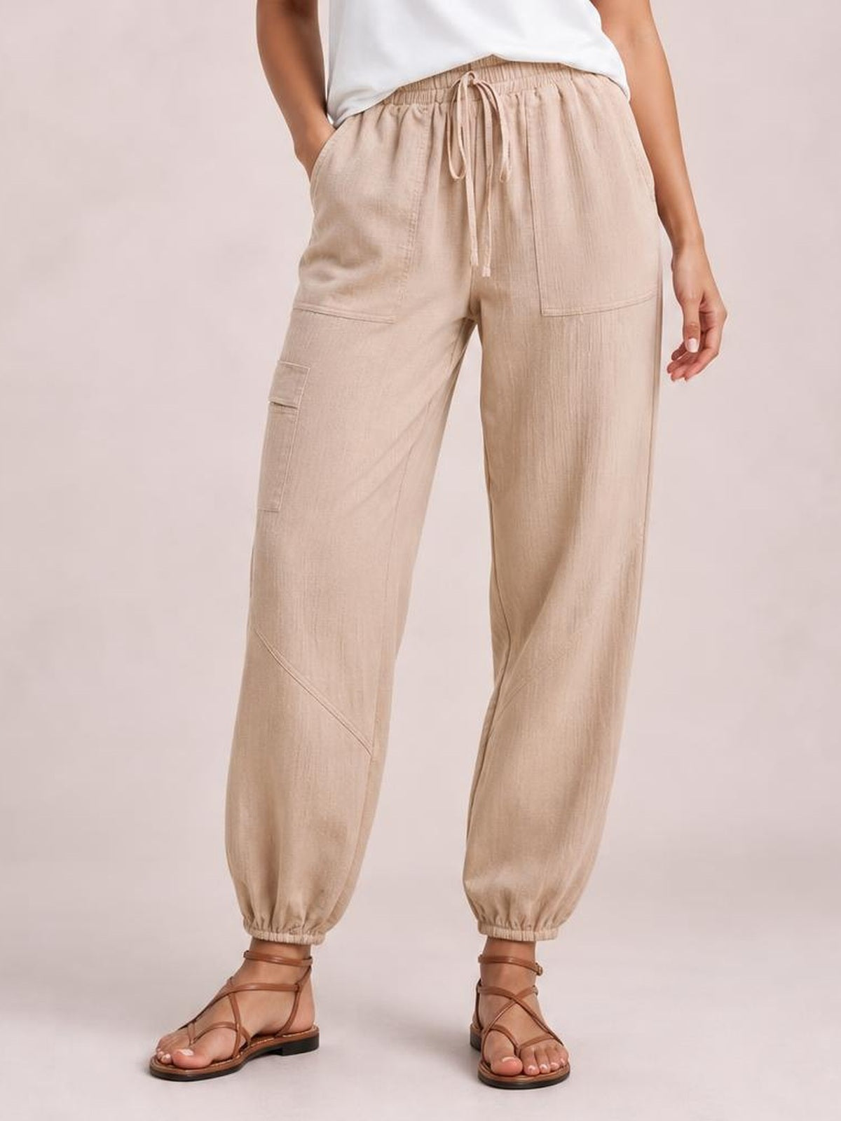 Model wearing beige elastic waist joggers with a drawstring, roomy straight-leg silhouette, cargo-style pockets, and gathered ankle cuffs.