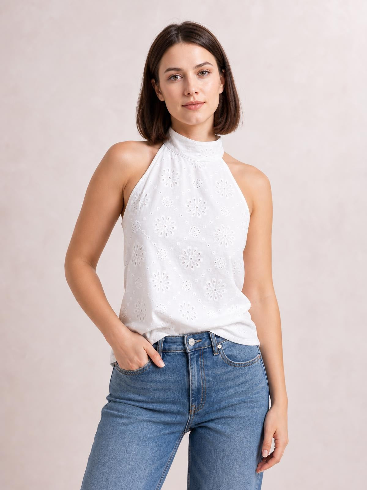 A model wears a white eyelet Grecian neck tank with a high neckline, sleeveless cut, relaxed silhouette, and floral cutout construction.