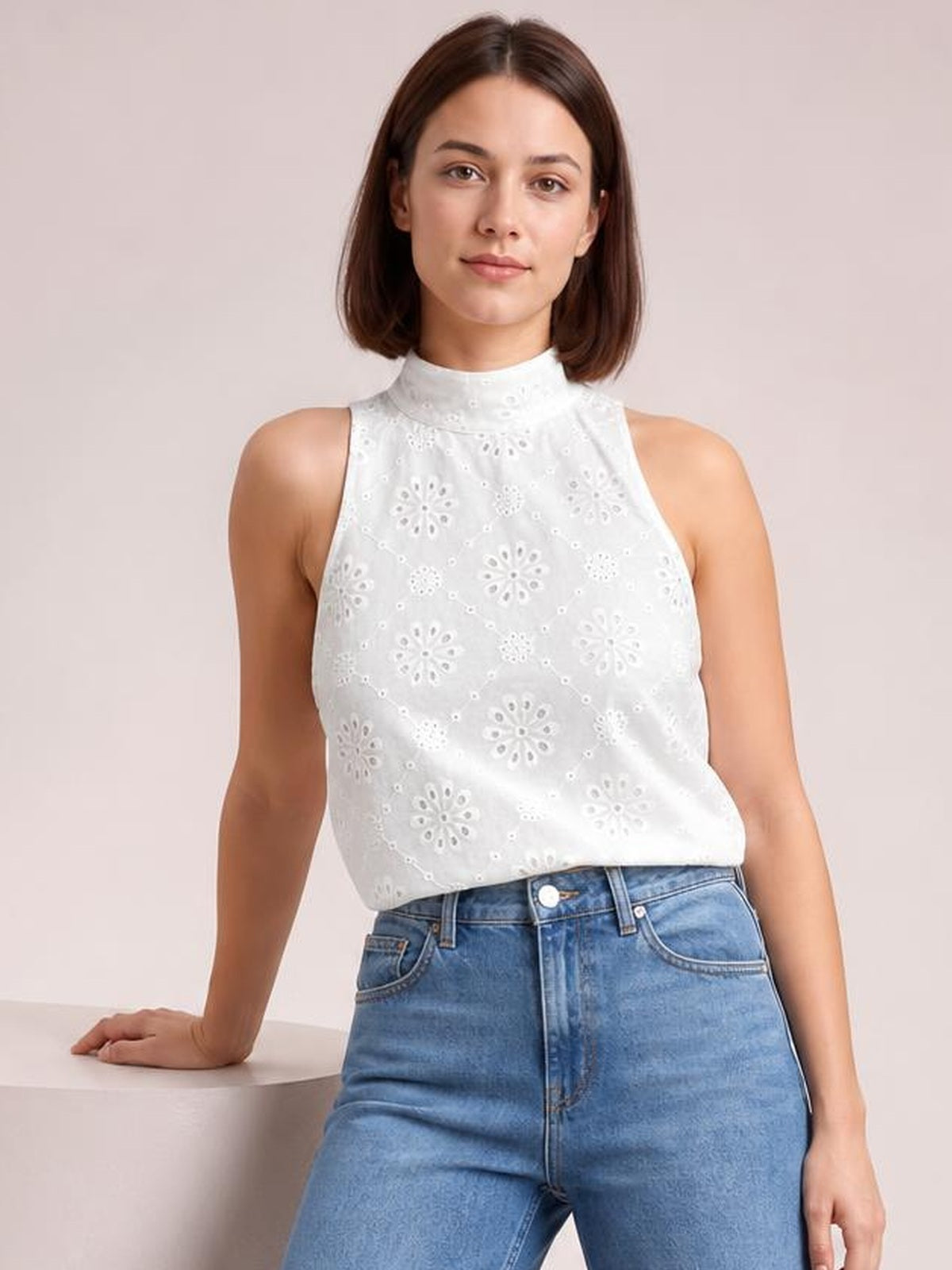 A model wears a white eyelet Grecian neck tank with a high neckline, sleeveless cut, relaxed straight silhouette, and delicate floral cutout construction.