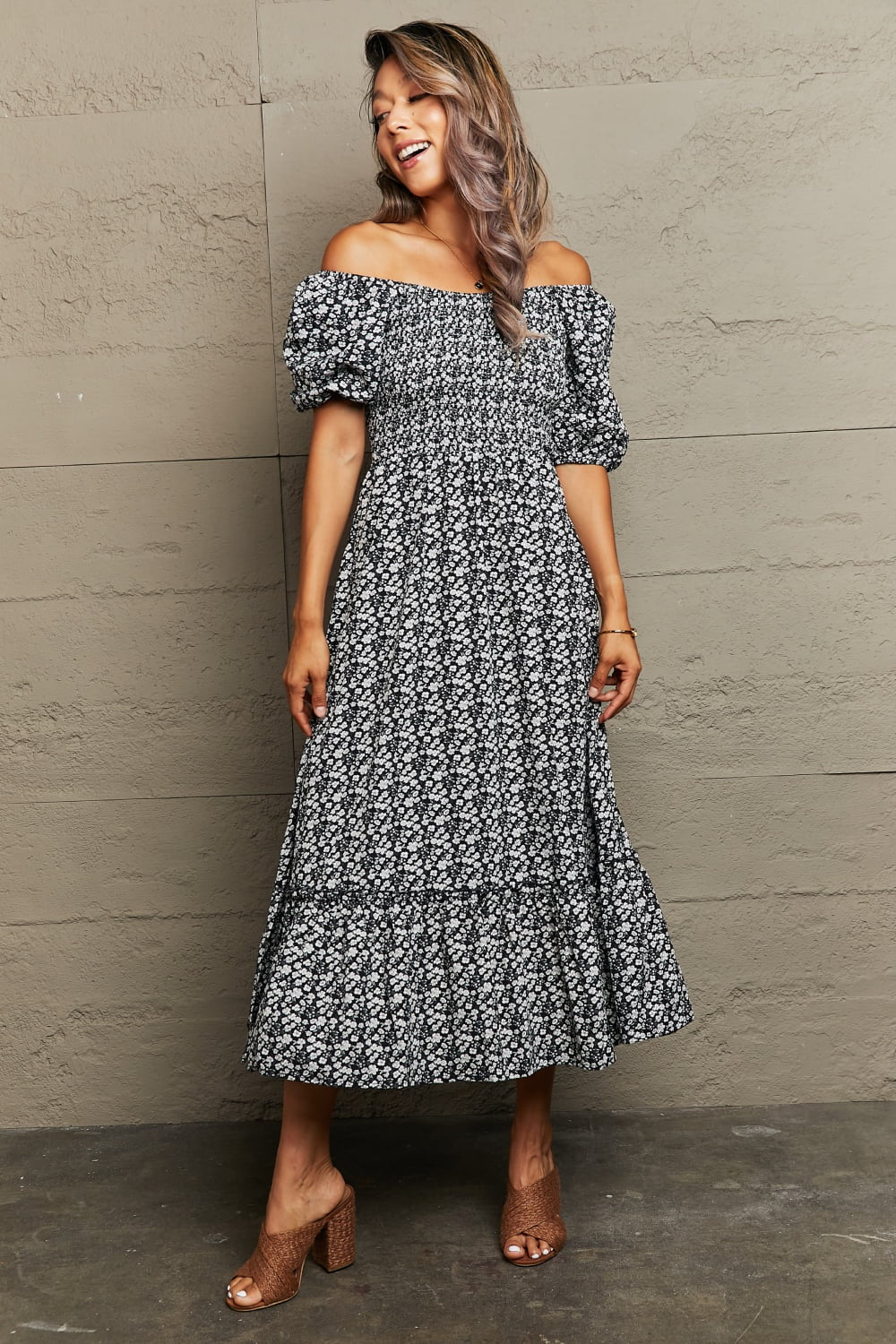 A model stands in a black floral midi dress with an off-shoulder square neckline, short puff sleeves, gathered waist, and flowing A-line silhouette.
