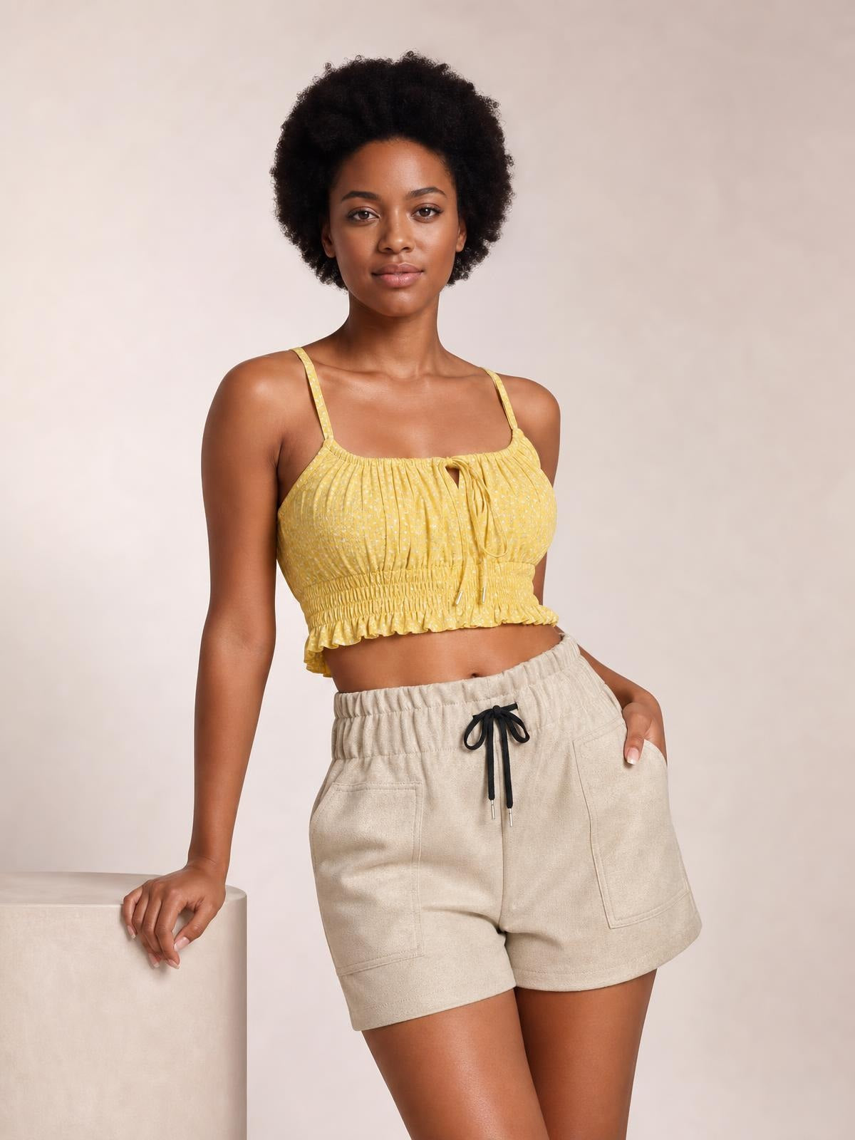 A model poses in beige drawstring shorts with an elastic waistband, relaxed straight-leg silhouette, and large front patch pockets, holding one pocket.