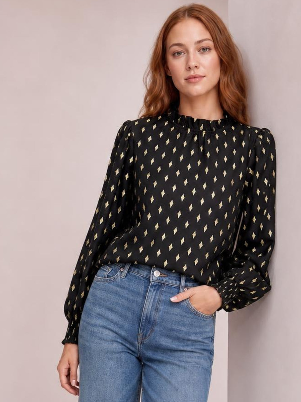 Model poses in a black geometric print blouse with a frill neck, smocked detail, regular fit, and long puff lantern sleeves, paired with jeans.