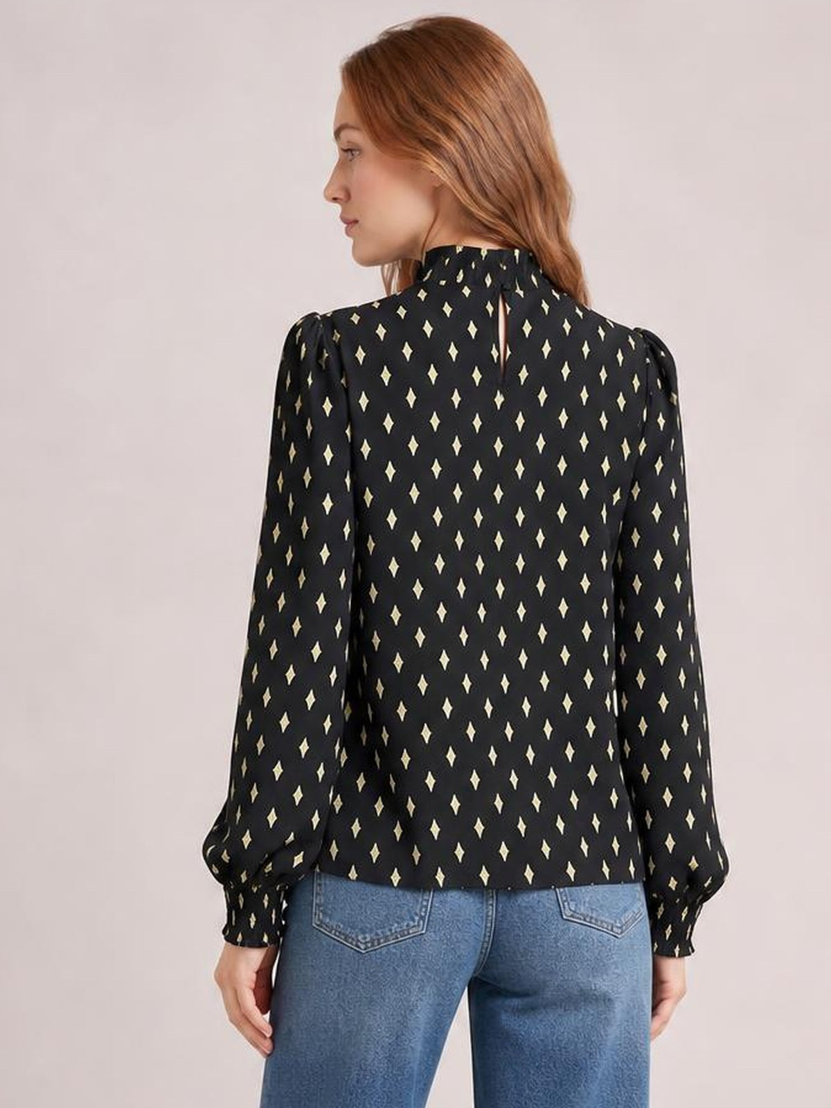 Model shown from the back wears a black geometric print blouse with a high frill neck, puffed lantern sleeves, smocked cuffs, and a regular silhouette.
