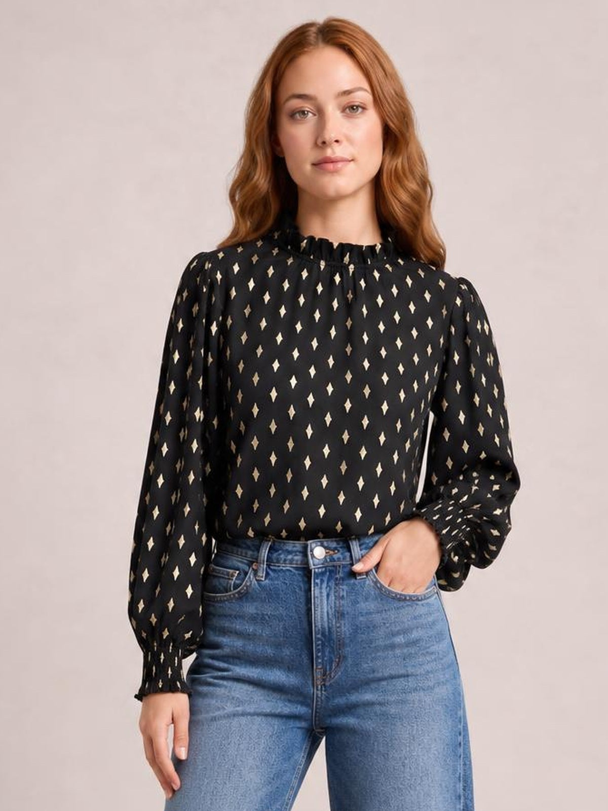 Model stands with one hand in her jeans pocket, wearing a black geometric-print blouse with a frill neck and long lantern sleeves with gathered cuffs.