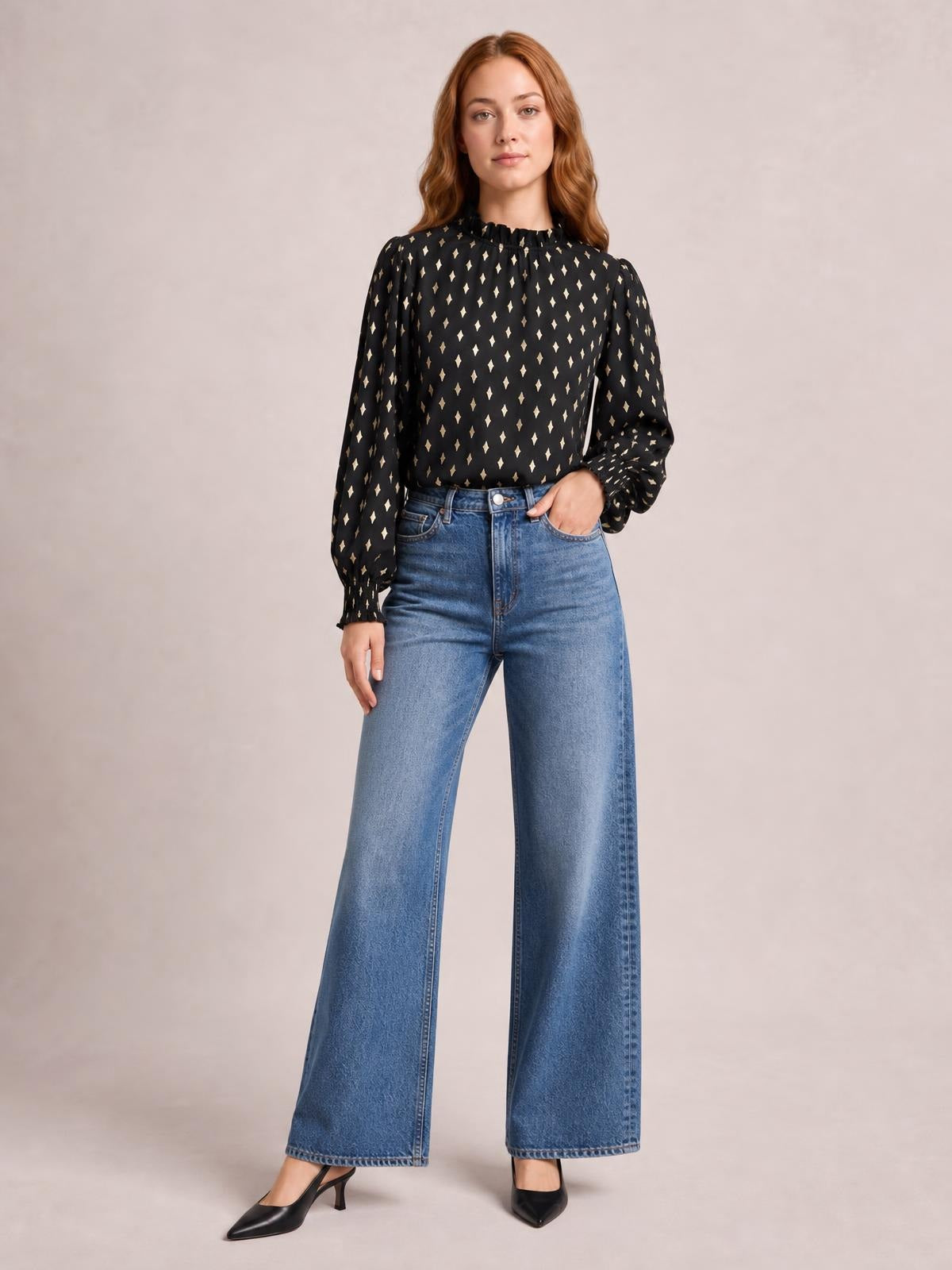 A model stands in a black geometric-print blouse with a frill neck, smocked detailing, and long lantern sleeves with gathered cuffs.