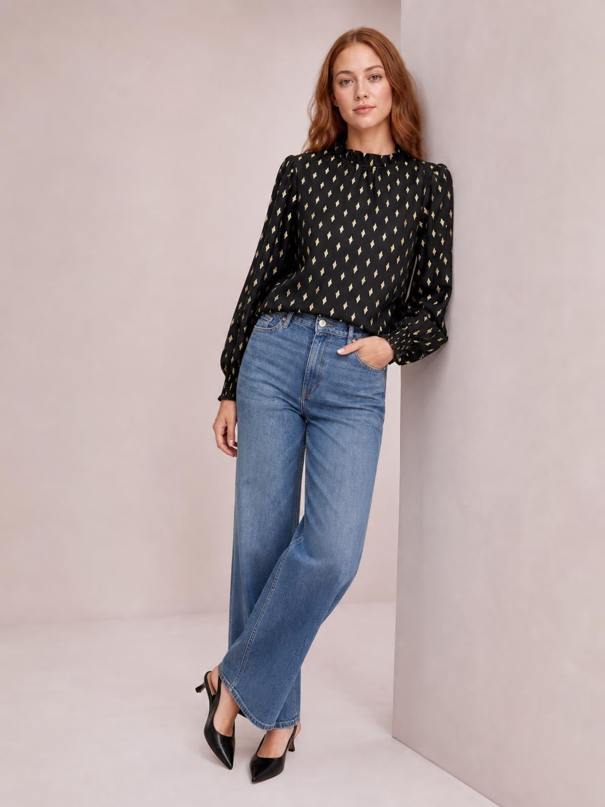 Model poses in a black geometric print blouse with a frill neck, smocked detailing, long puff sleeves, and a relaxed regular-length silhouette.