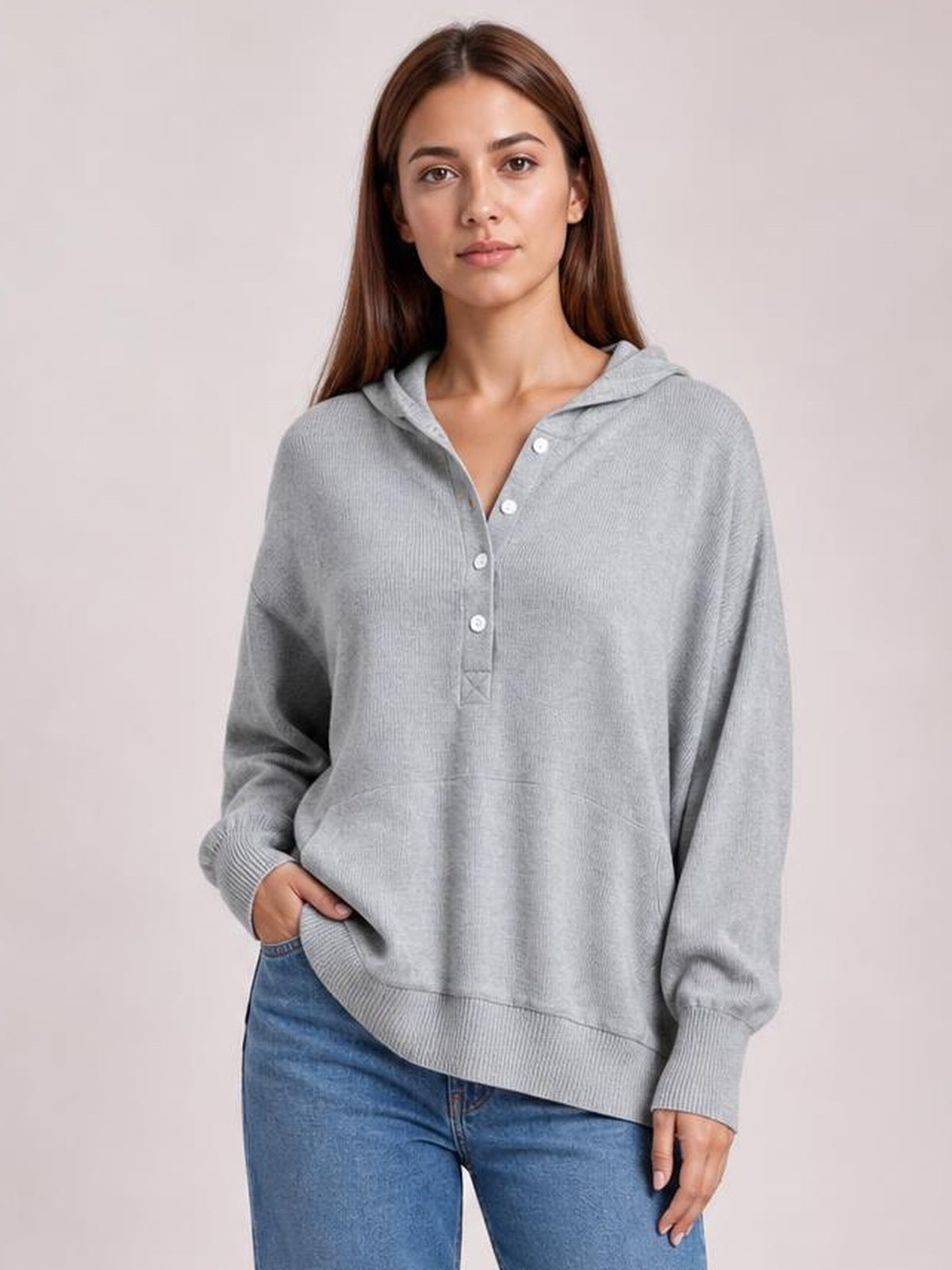 A model stands in a relaxed gray half-snap long sleeve hoodie with a hood, button placket, ribbed cuffs and hem, and an easy oversized silhouette.