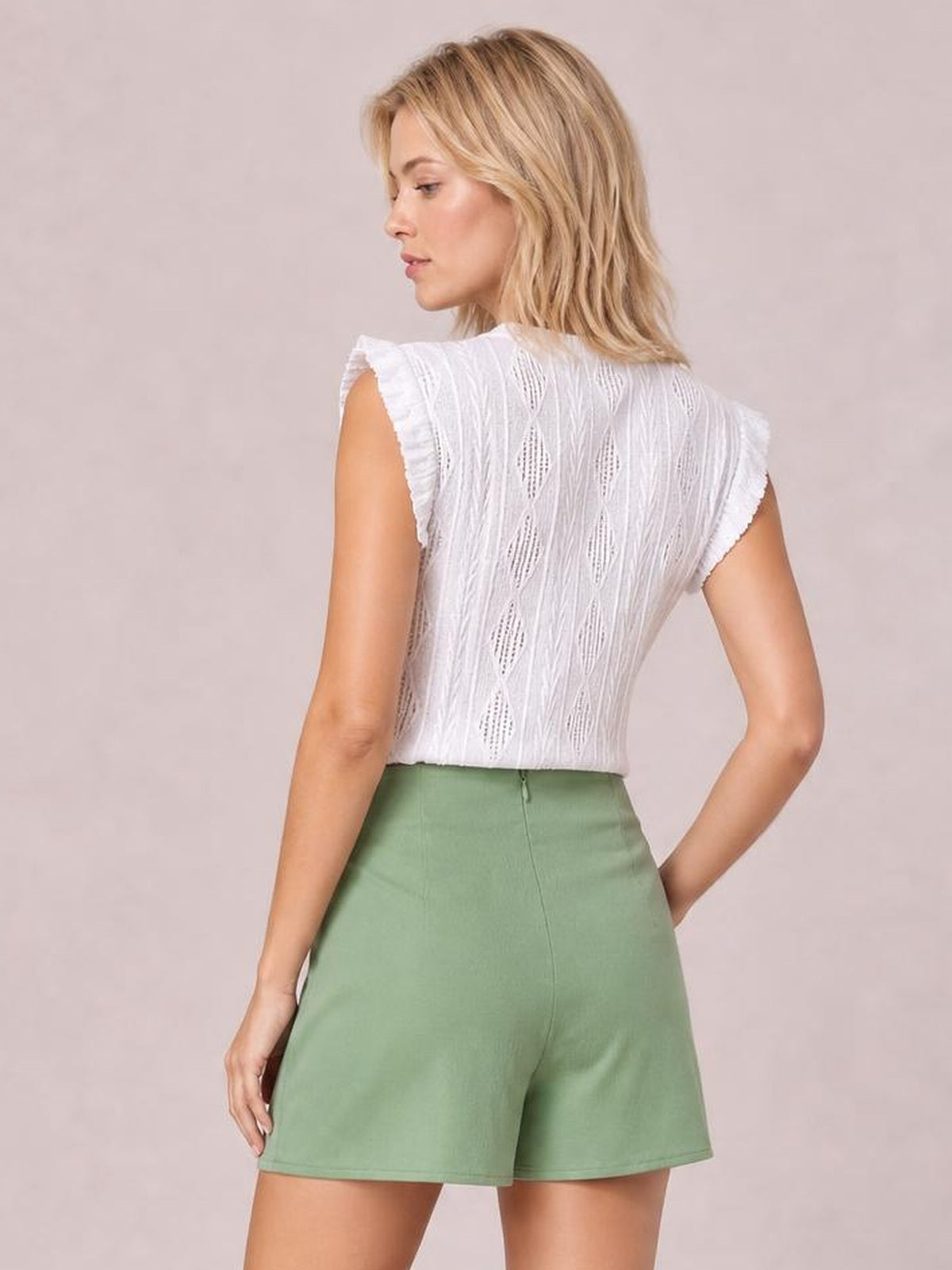 A model poses from the back in a sage green high waist skort with an opaque, tailored shorts silhouette and visible center-back seam.