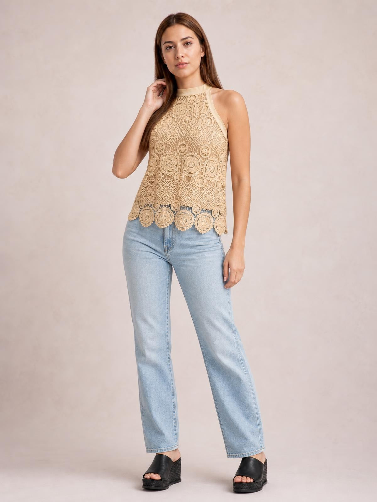 A model poses with one hand near her hair in a beige lace mock neck tank featuring a sleeveless cut, relaxed silhouette, and scalloped hem.