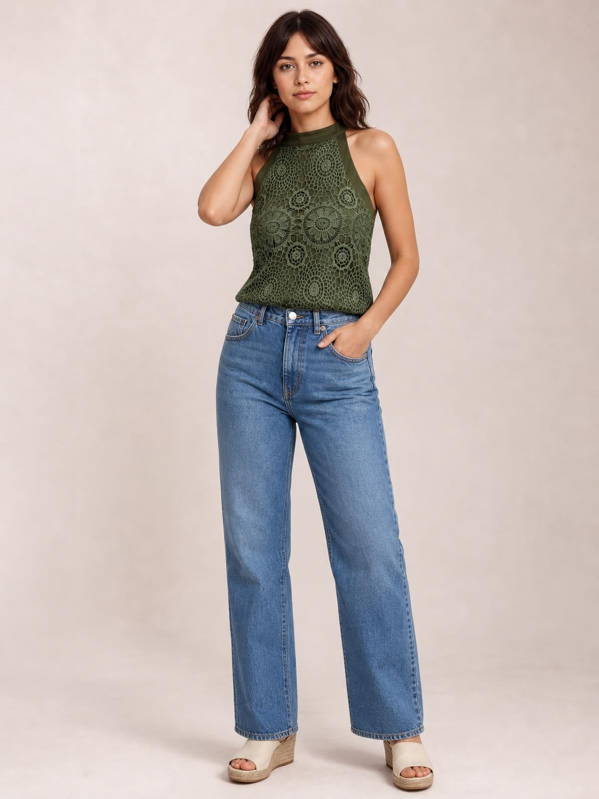 Model wears an olive green lace mock neck tank with a sleeveless cut, opaque floral construction, and a relaxed straight silhouette, posing with one hand at her neck.